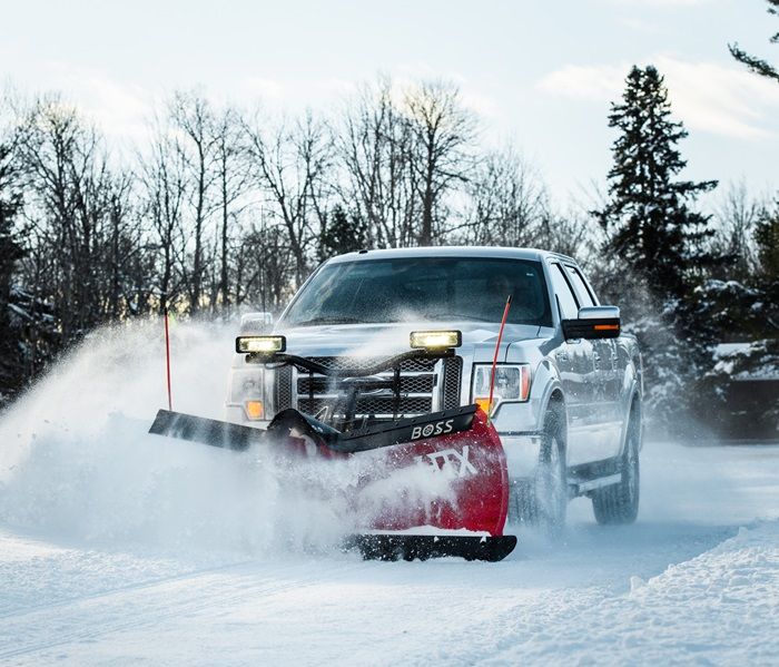 Silver pickup truck with red BOSS snowplow clearing snow on a winter road