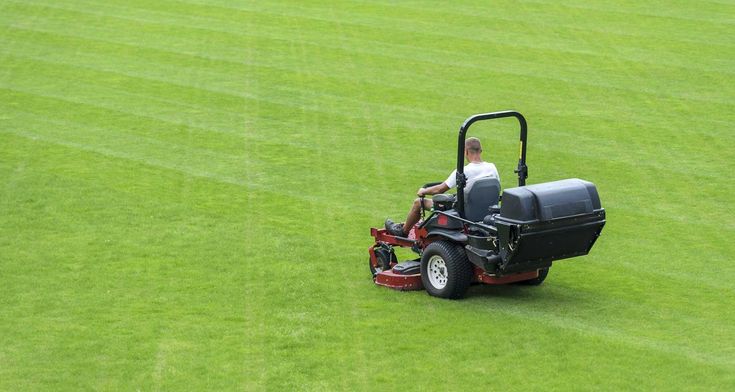 Professional riding lawnmower creating striped patterns on a large commercial lawn